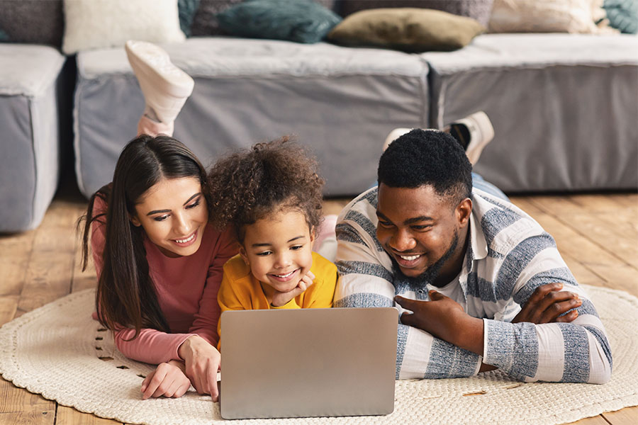 Blog - Happy Parents and Daughter Laying on Floor in Living Room Using Their Laptop