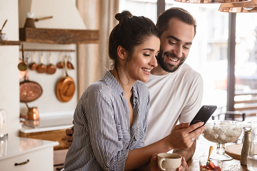 Client Center - Happy Young Couple Standing in Kitchen Using Their Phone